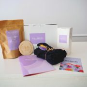 Die drei grundlegenden Wochenbett-Helferlein: Kühlbinden, elastische Unterwäsche und “Peri Bottle" mit Wochenbett-Kräutertee und einen dekorative Holzscheibe mit der Aufschrift “Hello World”.