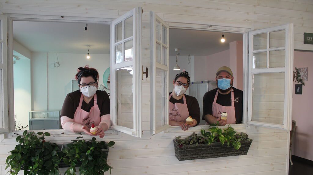 Sabrina Eßlinger, Isabell Schremmer und Manuel Jonik schauen durch die selbstgebaute Trennwand im Laden, die das Café vom hinteren Bereich des Ladens trennt, in dem Beratungsgespräche zu Torten stattfinden. © Julia Wadle